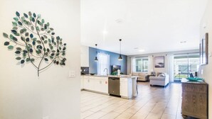 A modern kitchen with white cabinets, a dishwasher, and a dining area with a white table and chairs. - 1669MVD Amazing Champions Gate 8 Bedroom 5 Bed Villa by RedAwning (Davenport)