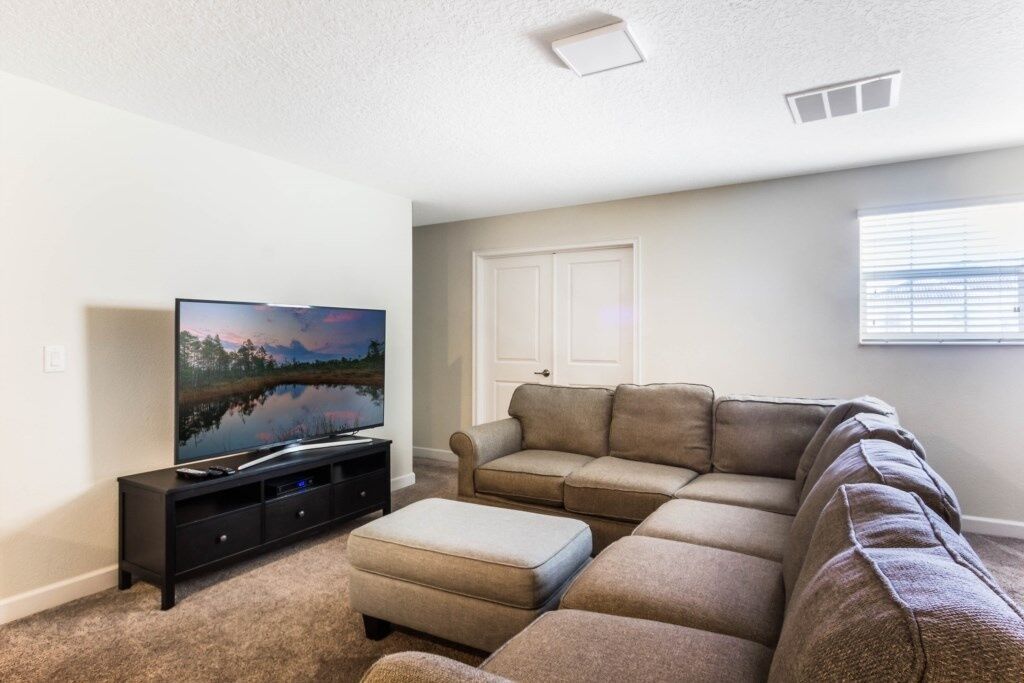 A living room with a sectional sofa, a TV on a stand, and a door in the background.