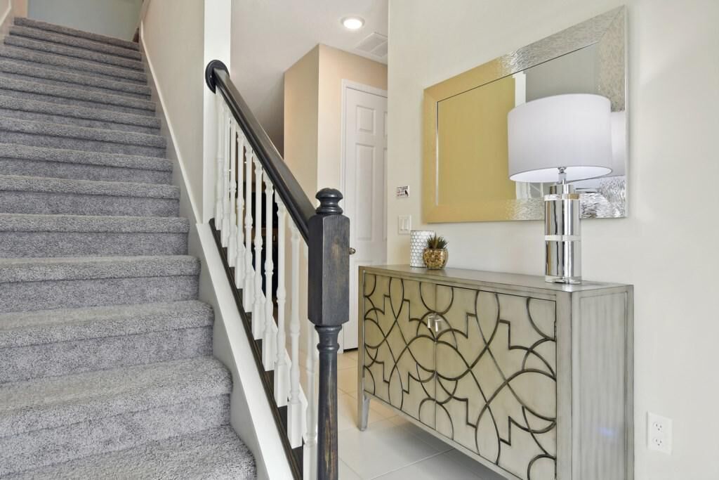 A staircase with a black handrail and white balusters, leading to a room with a white door and a decorative cabinet with a gold pattern.