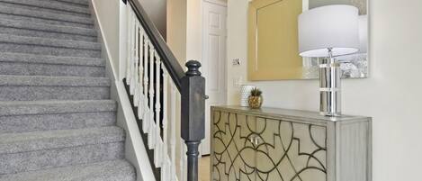 A staircase with a black handrail and white balusters, leading to a room with a white door and a decorative cabinet with a gold pattern.