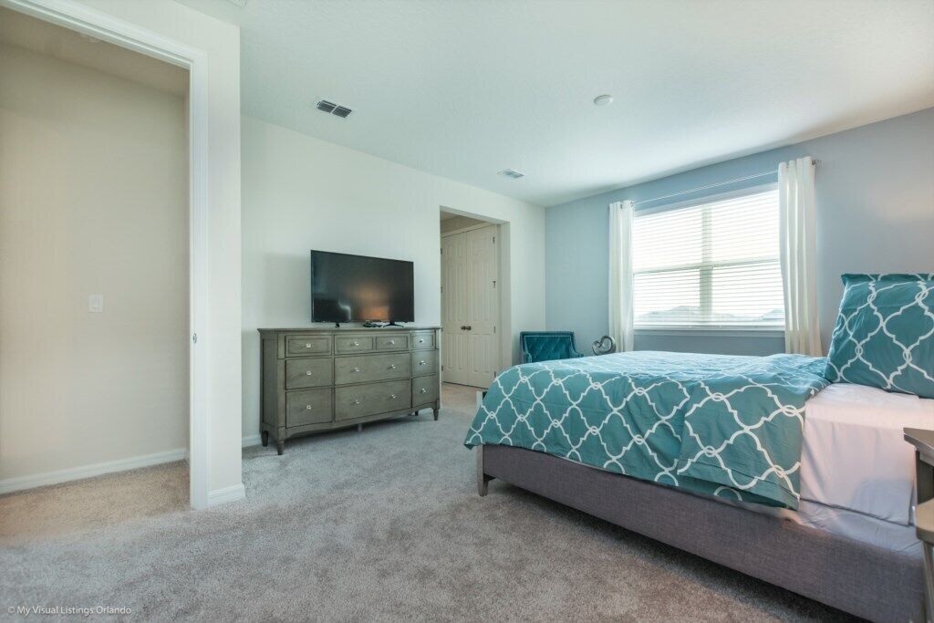 A bedroom with a bed, dresser, TV, and a window with curtains.