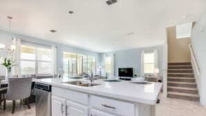 A spacious kitchen with a large island, white cabinetry, and a dining area with a table and chairs. - 1791spp 5 Bedroom Townhouse by RedAwning (Kissimmee)