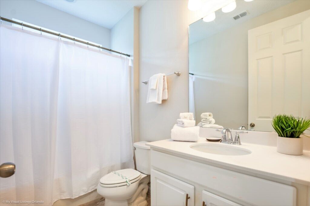 A bathroom with a shower curtain, a toilet, a sink, a mirror, and a potted plant.