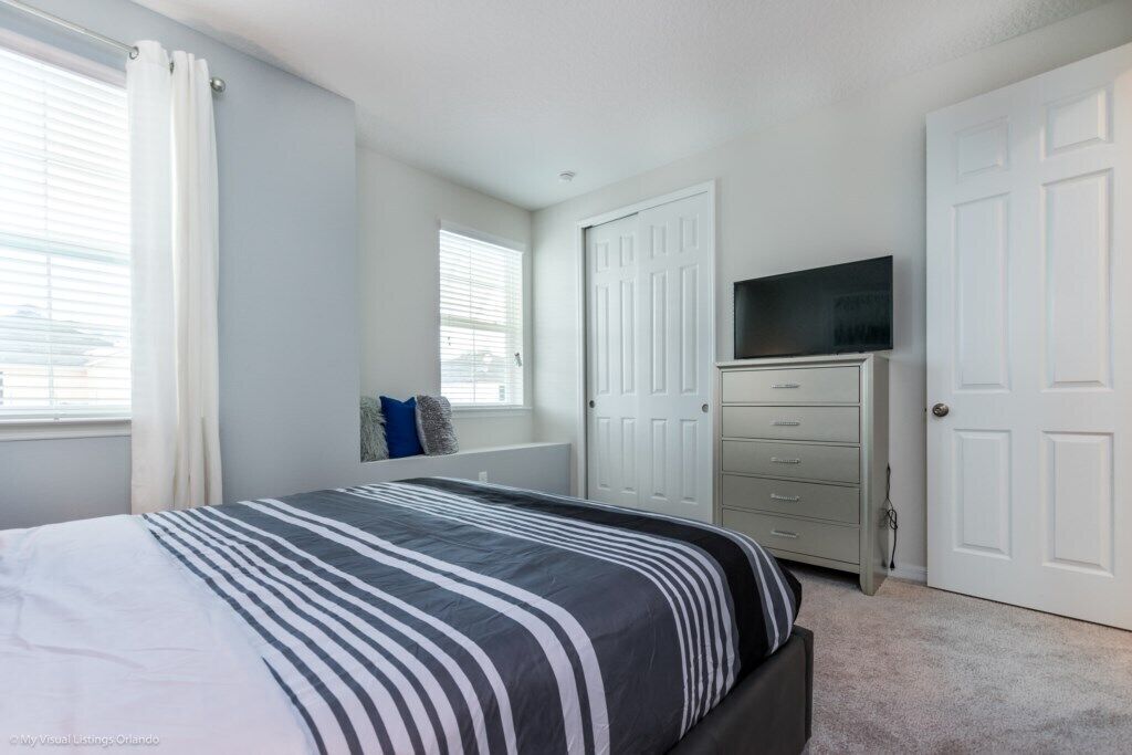 A bedroom with a bed, a dresser, a television, and a closet.