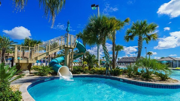 A swimming pool with a water slide, palm trees, and a clear blue sky. - Gorgeous Townhome In Champion's Gate Near Disney! 4 Bedroom Townhouse by RedAwning (Davenport)