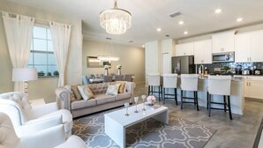 A modern living room with a sofa, chairs, a coffee table, and a kitchen area with bar stools. - Gorgeous Townhome In Champion's Gate Near Disney! 4 Bedroom Townhouse by RedAwning (Davenport)