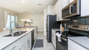 A modern kitchen with stainless steel appliances, a double sink, and a large island. - Gorgeous Townhome In Champion's Gate Near Disney! 4 Bedroom Townhouse by RedAwning (Davenport)