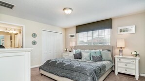 Een slaapkamer met een groot bed, twee nachtkastjes, een dressoir, een raam met zonwering en een deur.