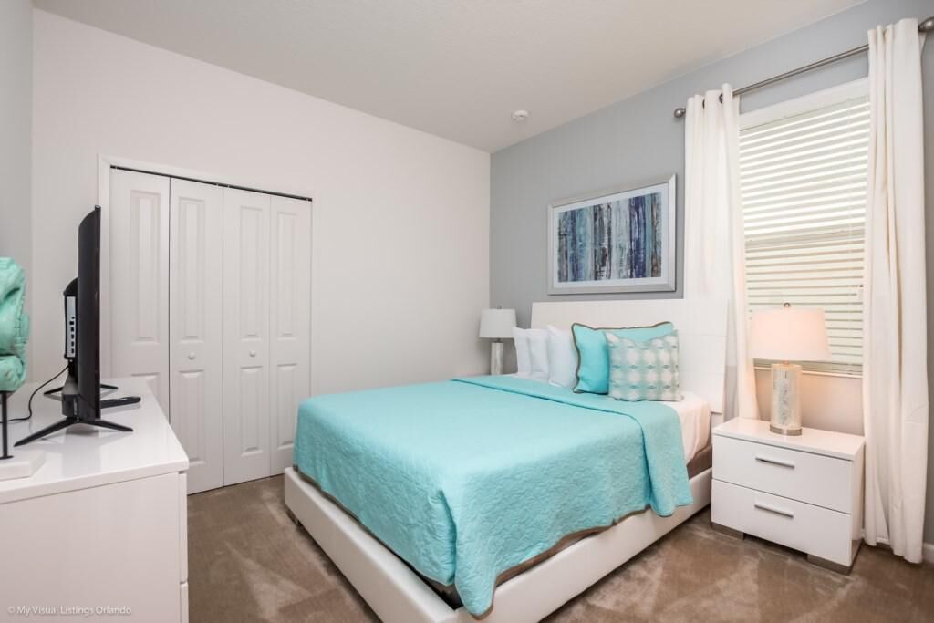 A bedroom with a bed, a nightstand, a desk, a television, and a wardrobe.