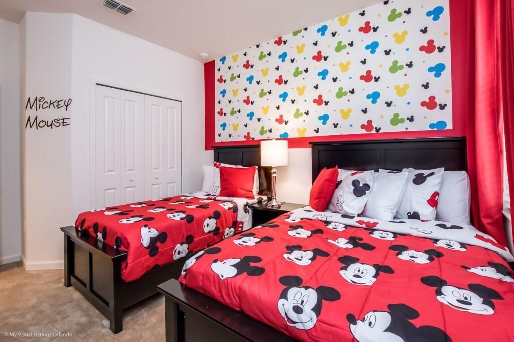 A Mickey Mouse themed bedroom with two beds, red bedding, and a colorful wall mural.