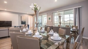 A modern dining area with a glass table set for a meal, surrounded by comfortable seating. - 2619ca 10 Bedroom Villa by Redawning (Kissimmee)