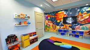 Ein Spielzimmer für Kinder mit farbenfrohem Wandgemälde, Regalen voller Spielzeug, einem Spieltisch und einem Sitzsack.