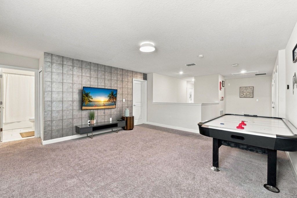 Une pièce équipée d’une table de billard, d’un téléviseur à écran plat fixé sur un mur texturé et d’une porte donnant sur une autre pièce.