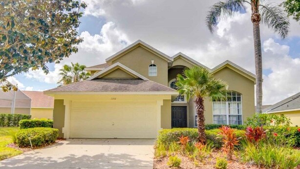 A two-story house with a garage, surrounded by well-maintained landscaping and a palm tree. - Privacy Pool Area In This Beautiful ! 4 Bedroom Home by RedAwning (Haines City)