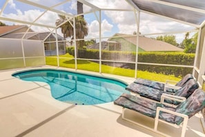 A covered swimming pool with lounge chairs and a view of a well-maintained lawn and house.