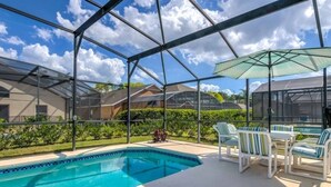 Piscina ao ar livre coberta com estrutura de vidro, rodeada por um terraço com cadeiras e mesa.