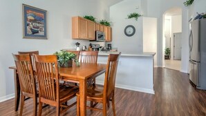 Uma sala de jantar com uma mesa e cadeiras de madeira, uma cozinha com armários de madeira e um micro-ondas, e uma geladeira.