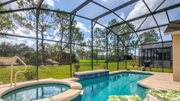 Une piscine extérieure couverte avec un jacuzzi, entourée d’une structure en verre, et un espace patio aménagé avec du mobilier d’extérieur.