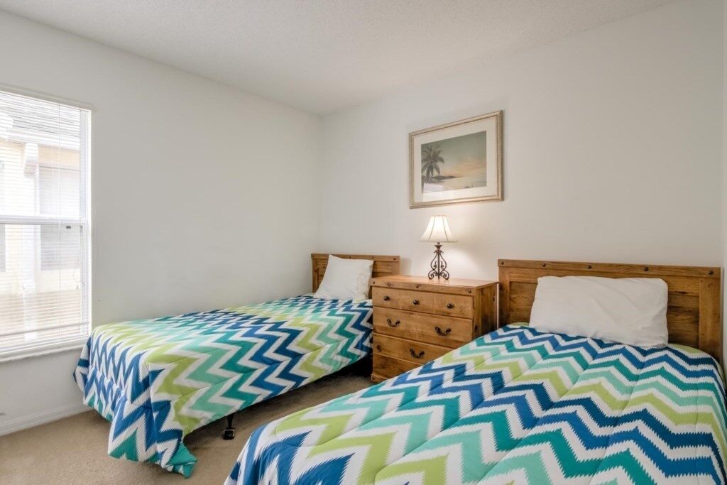 A bedroom with two single beds, a wooden dresser, a nightstand with a lamp, and a framed picture on the wall.