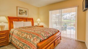 A bedroom with a wooden bed, two bedside tables, a large window with blinds, and a view of a pool.