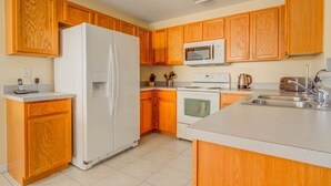 A kitchen with wooden cabinets, a white refrigerator, a microwave, an oven, and a sink.