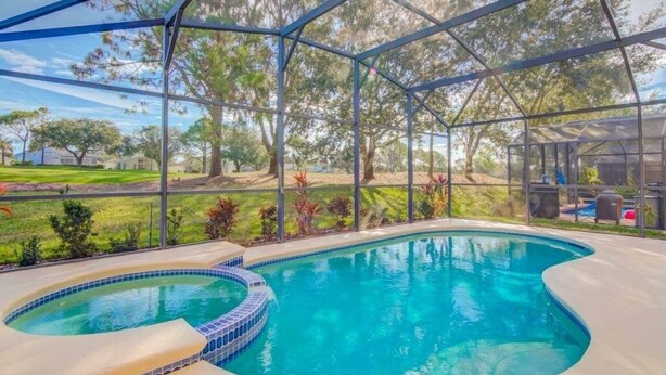 A swimming pool with a hot tub, surrounded by a covered area with a view of a landscaped garden and trees.
