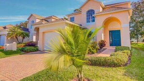 A residential house with a central archway, a blue door, and a well-maintained garden with palm trees.