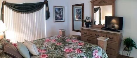 Une chambre à coucher avec un lit, une commode, une télévision et un miroir.