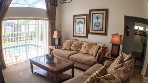 A living room with a sofa, a coffee table, and two lamps. There are two framed pictures on the wall. - South Facing Pool Great For Families! 4 Bedroom Home by RedAwning (Haines City)