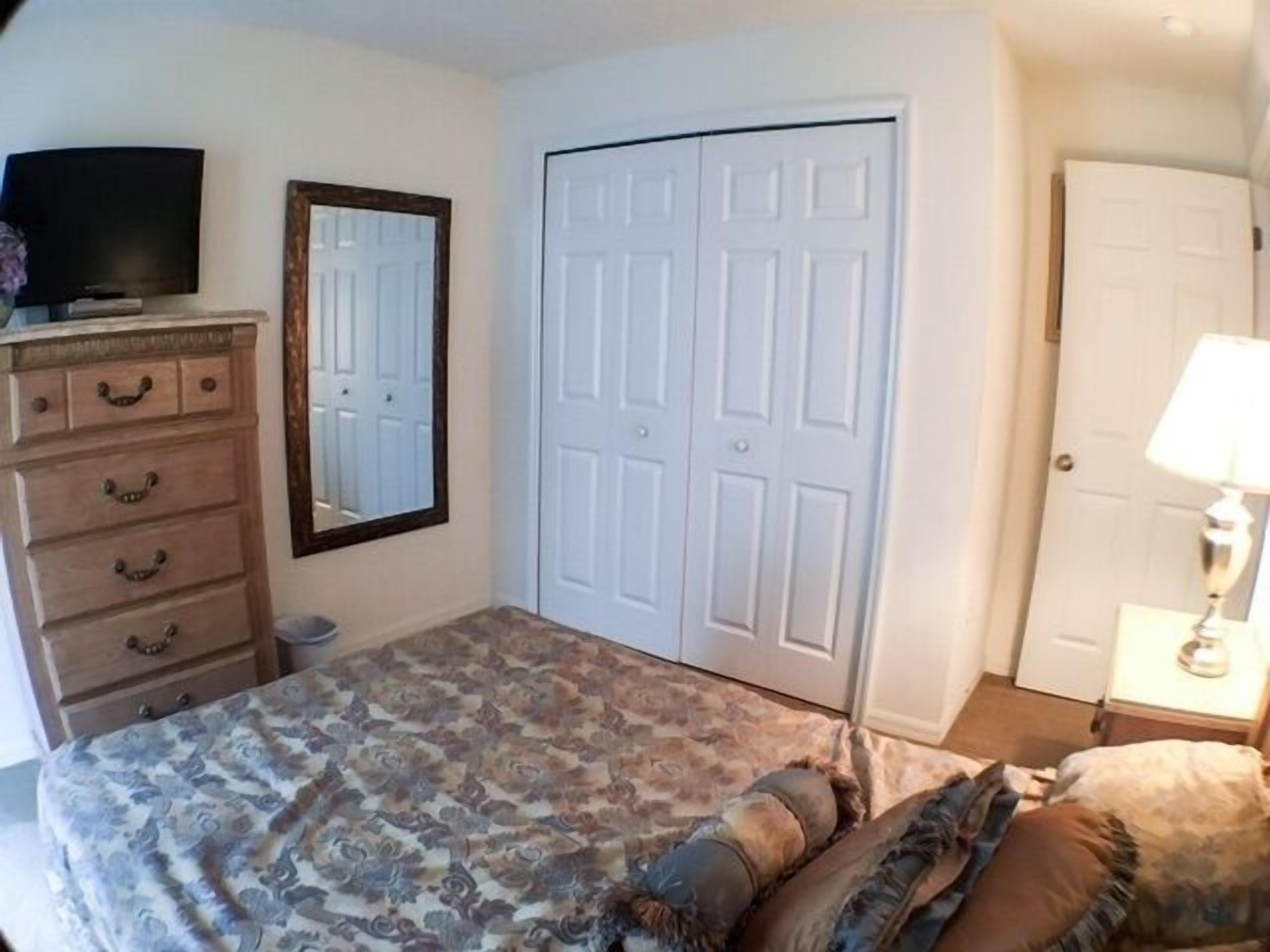A bedroom with a bed, dresser, mirror, wardrobe, and a TV.
