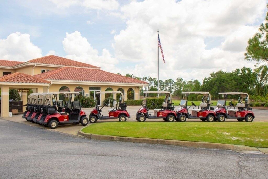 A building with a red-tiled roof, a flagpole with an American flag, and a row of golf carts parked in front.