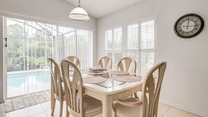 Un coin repas avec une table et des chaises en verre, de grandes fenêtres et une horloge au mur.