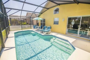 Piscina exterior coberta com cadeiras azuis e um guarda-sol.