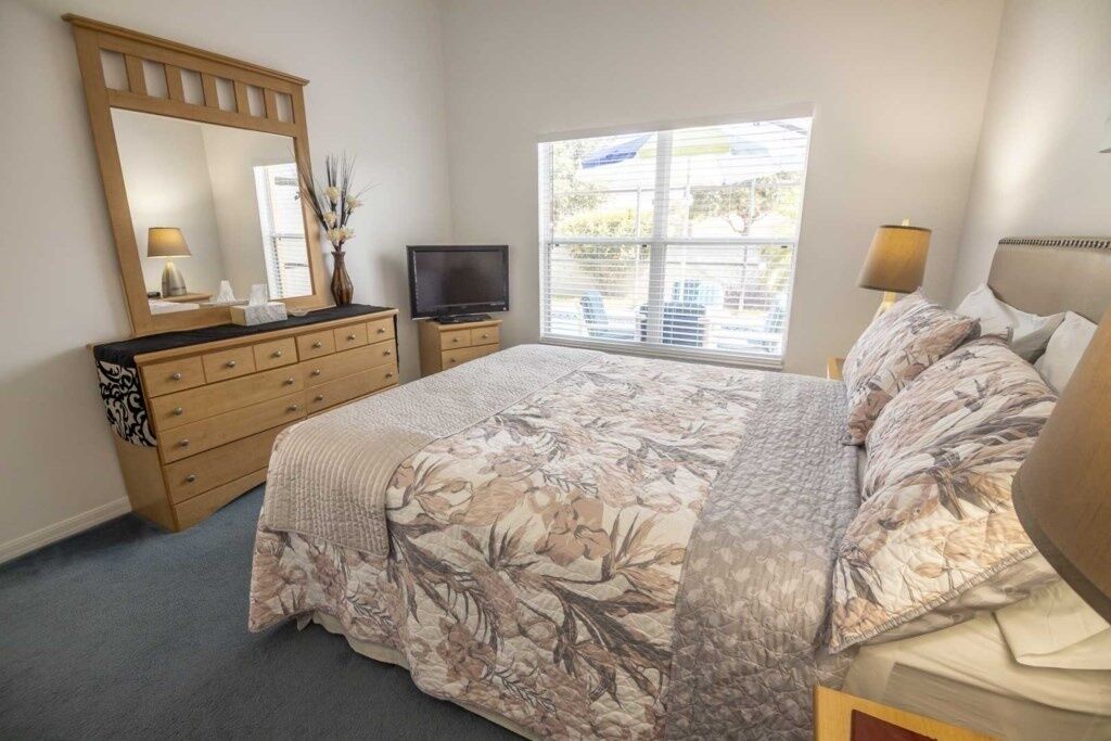 Un dormitorio con cama, cómoda, televisor y ventana con persianas.