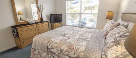 Un dormitorio con cama, cómoda, televisor y ventana con persianas.