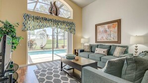 Un salon comprenant un canapé, une table basse et un téléviseur. Une fenêtre offre une vue sur une piscine et une terrasse.
