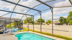 A covered outdoor swimming pool with a glass enclosure, lounge chairs, and a view of the neighborhood.