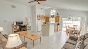 A spacious living area with a sofa, coffee table, and TV. A kitchen with wooden cabinets and a dining area with chairs are visible.