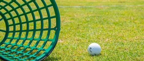 En golfbold på en græsplæne med et grønt golfklubbehoved i forgrunden.