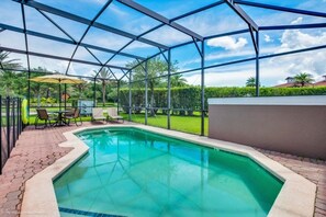 A swimming pool with a glass enclosure, surrounded by a patio area with chairs and a table. - Bella Vidatown With Full Size Pool! 4 Bedroom Townhouse by RedAwning (Kissimmee)