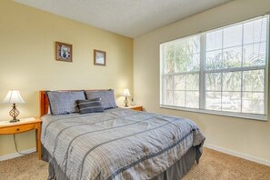 Une chambre avec un grand lit, deux tables de chevet avec des lampes, une fenêtre avec des stores et deux tableaux encadrés accrochés au mur.