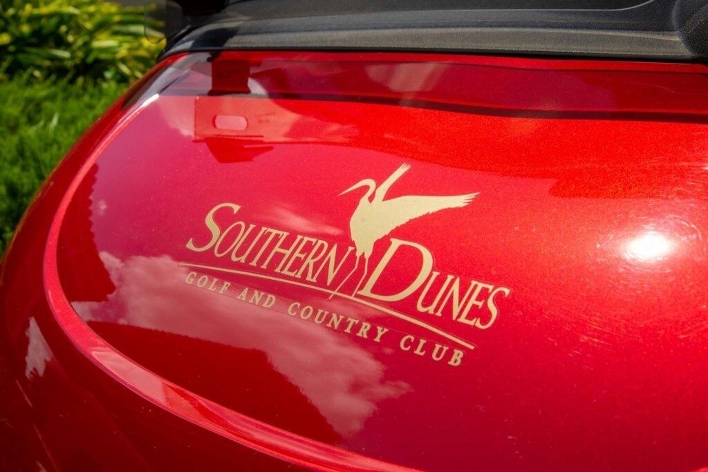 Un véhicule rouge arborant un logo et une inscription indiquant qu’il est associé à un club de golf et à un club de loisirs.