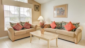 A living room with two beige sofas, a coffee table, and a window with blinds. - Gated Community Southern Dunes Golf 4 Bedroom Home by RedAwning (Haines City)