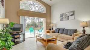A spacious living room with a large window, a sofa, a coffee table, and a television. - Gated Community Southern Dunes Golf 4 Bedroom Home by RedAwning (Haines City)