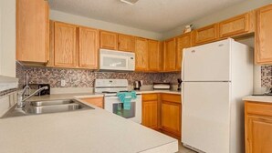 Eine Küche mit Holzschränken, einem weißen Kühlschrank, einer Mikrowelle und einer gefliesten Spritzschutzwand.