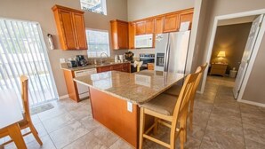 A kitchen with granite countertops, wooden cabinets, a central island, and a dining area with chairs.