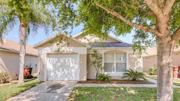 A single-story house with a garage, a front lawn, and a tree. - Southern Exposure Private Pool! 3 Bedroom Home by RedAwning (Haines City)