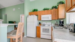 A compact kitchen with wooden cabinets, a white refrigerator, a microwave, and an oven. - Southern Exposure Private Pool! 3 Bedroom Home by RedAwning (Haines City)