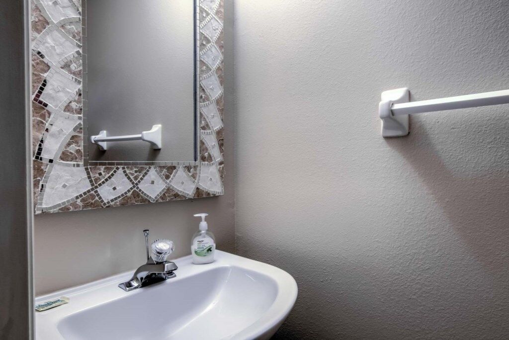 Un baño con lavamanos blanco, espejo y toallero.