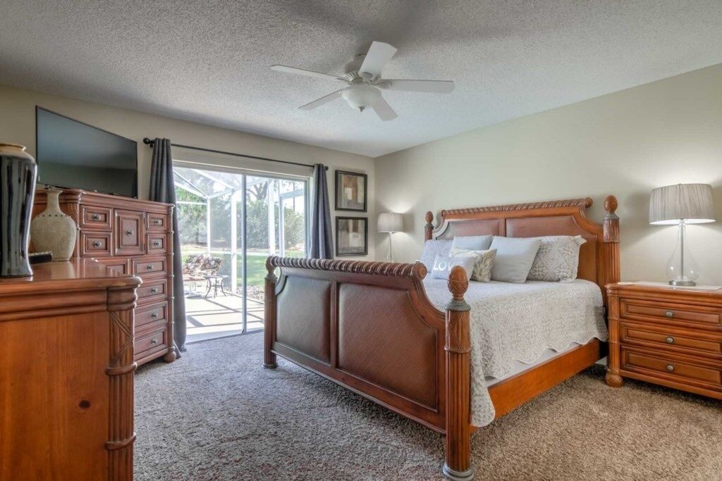 Une chambre à coucher avec un lit en bois, une commode, un téléviseur et un ventilateur de plafond.